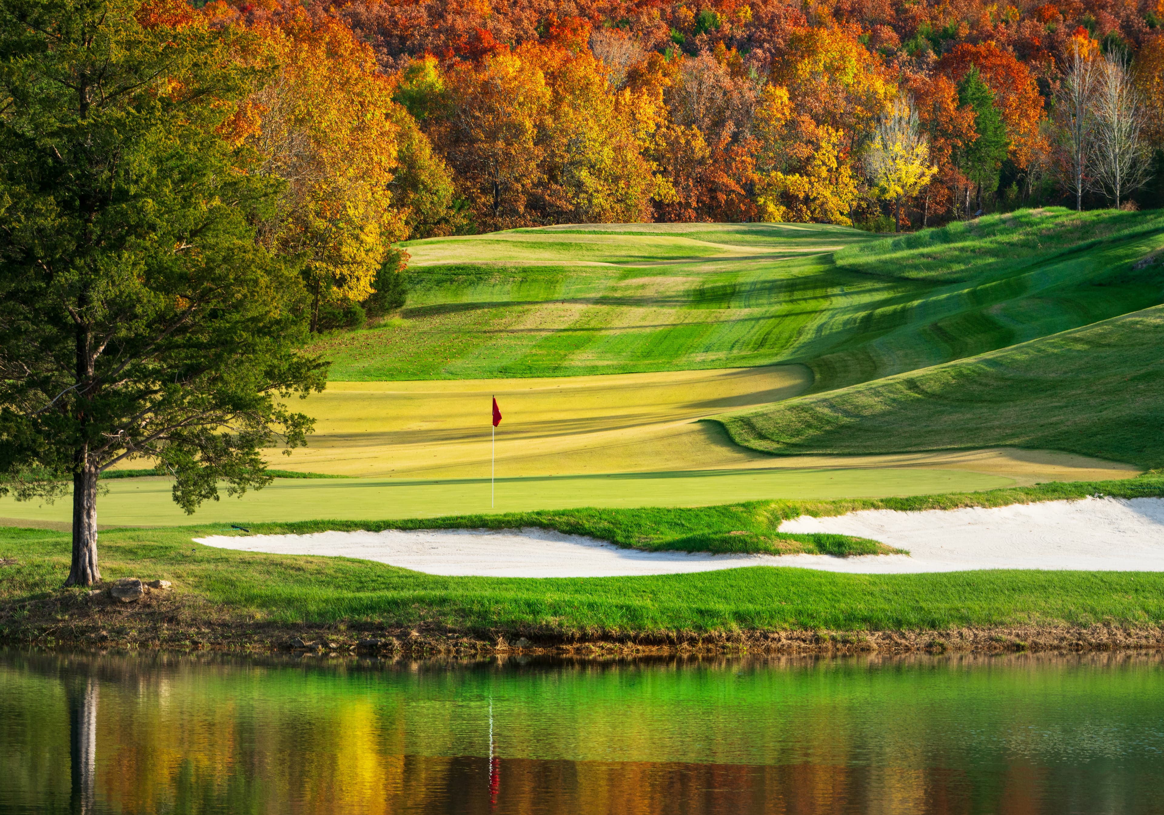 Buffalo Ridge Springs Golf Course in autumn with pond reflection and red flag on the green