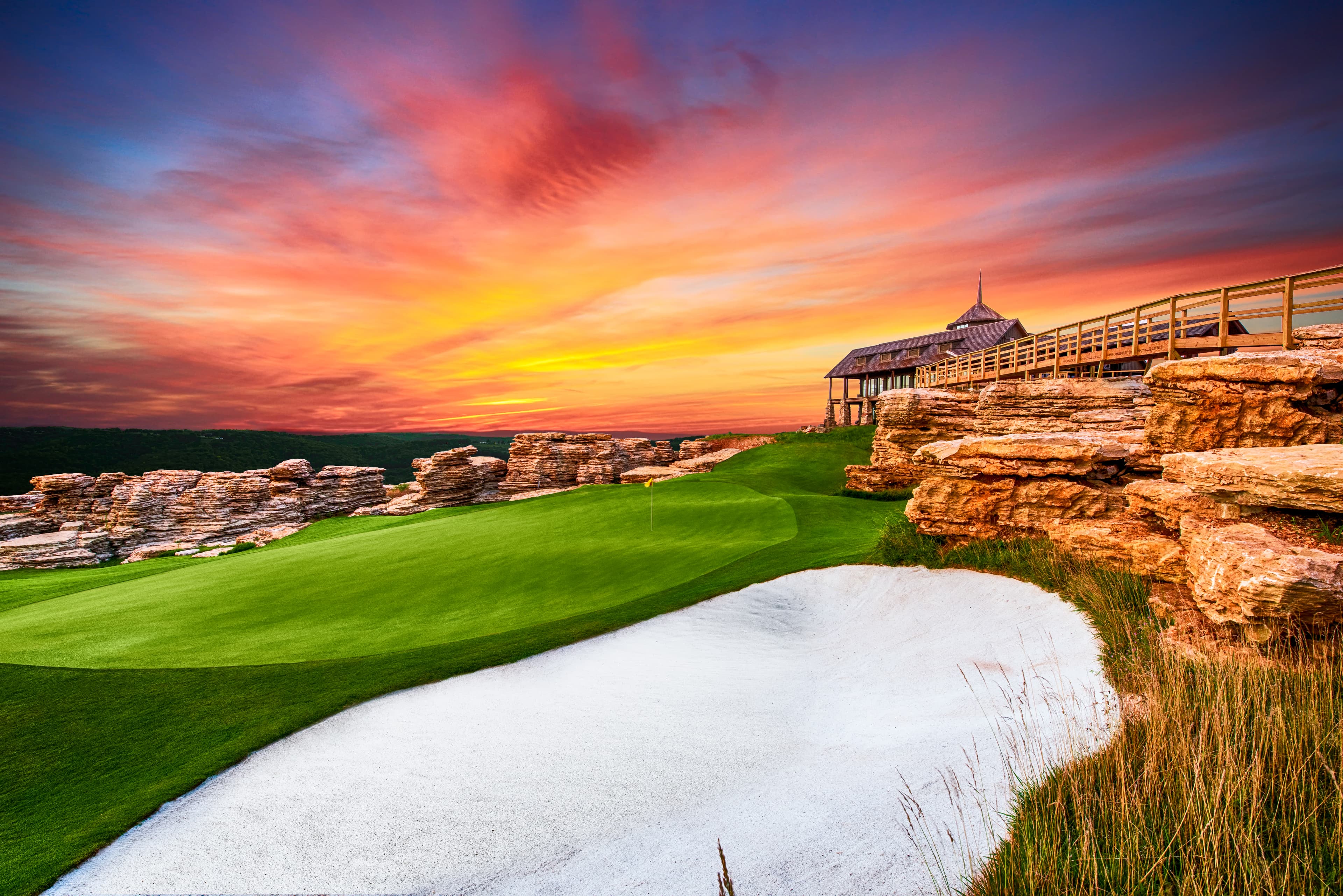 Mountain Top Golf Course hole 13 at sunset with dramatic rock outcrops, bunker, and clifftop pavilion
