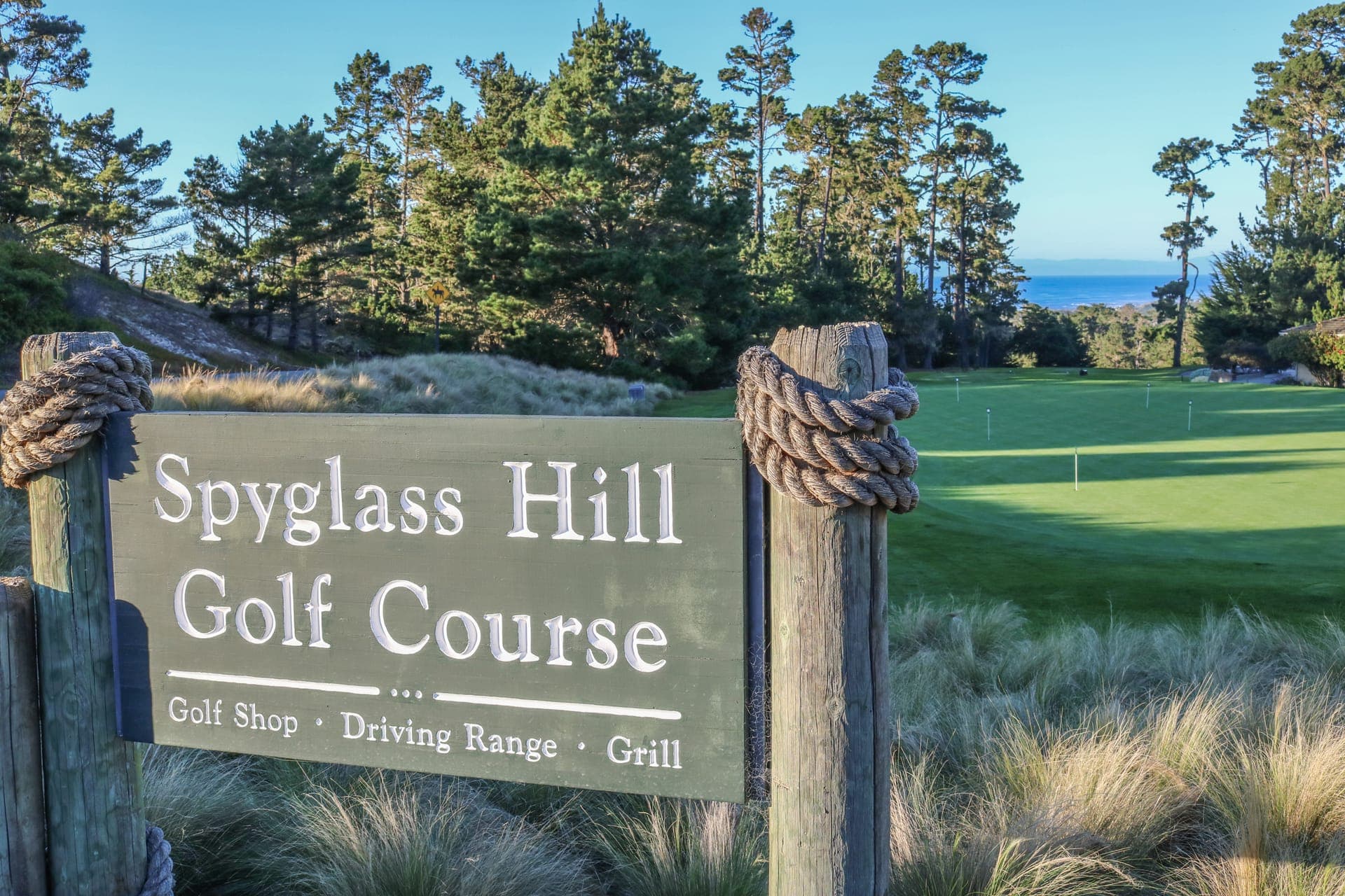 Wooden Spyglass Hill Golf Course entrance sign amid Monterey cypress and dunegrass