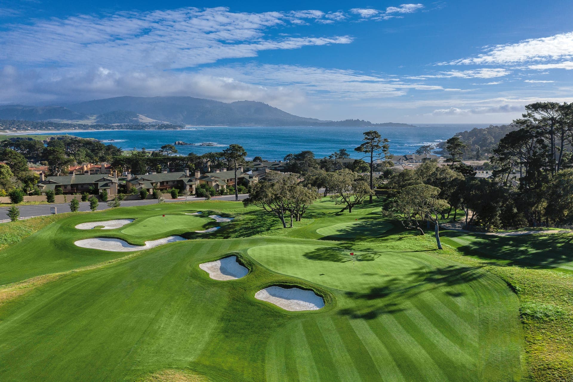 Aerial view of The Hay Short Course at Pebble Beach showing multiple greens, bunkers and oceanfront cottages above Carmel Bay