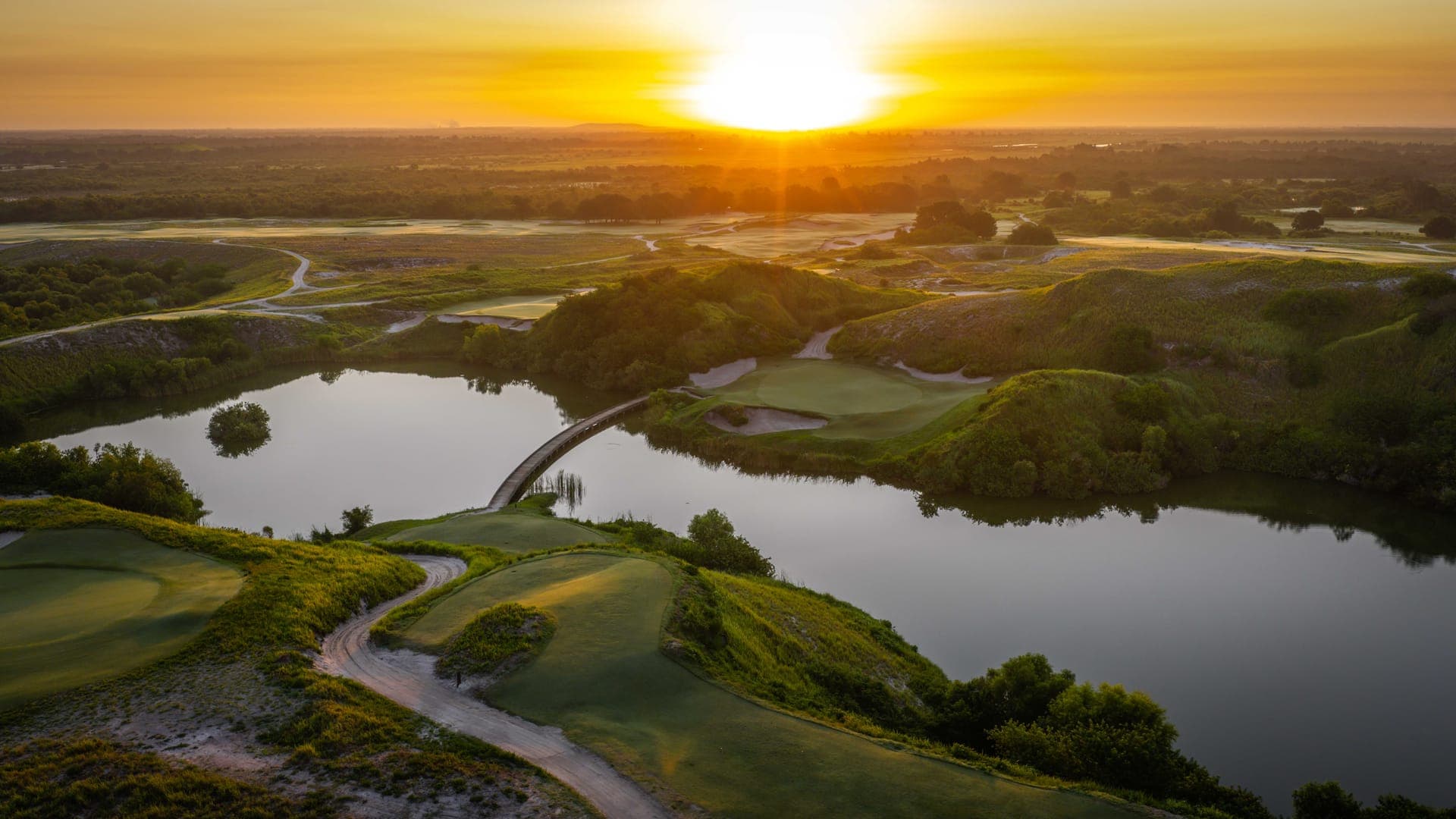 Aerial sunset view of Streamsong Resort with a boardwalk bridge crossing a lake on the Red course, central Florida