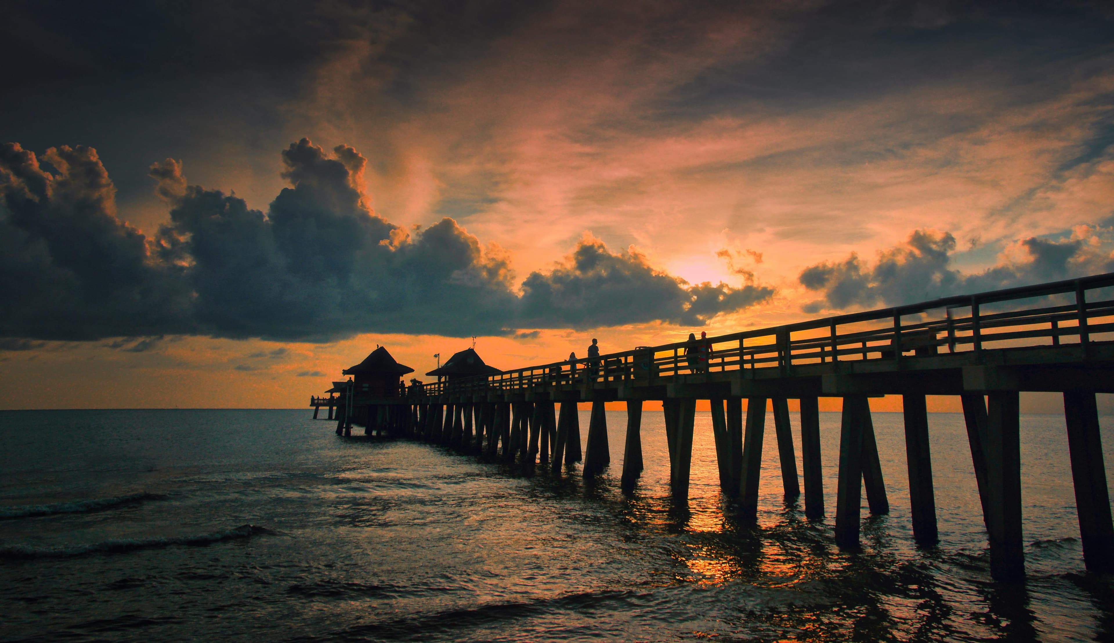 Naples Pier silhouetted against a dramatic sunset over the Gulf of Mexico