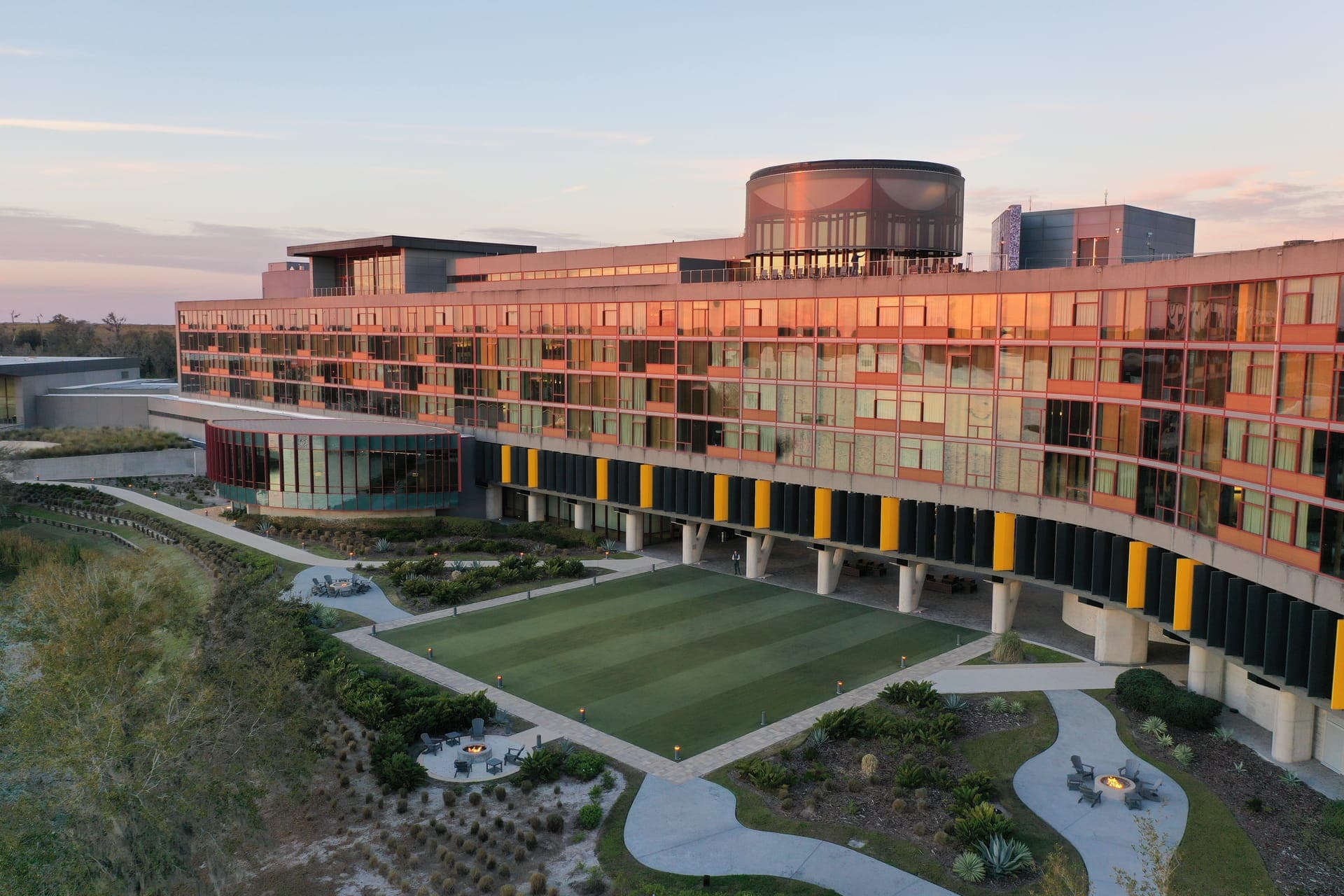 Aerial of the Streamsong Lodge at golden hour with a copper-glass facade and a putting-green courtyard with fire pits