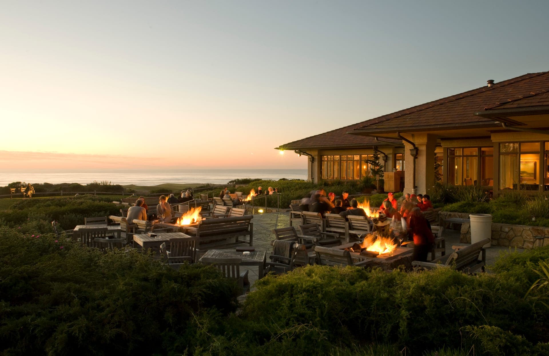 Guests gathered around firepits on the terrace at The Inn at Spanish Bay at sunset with the Pacific horizon glowing gold