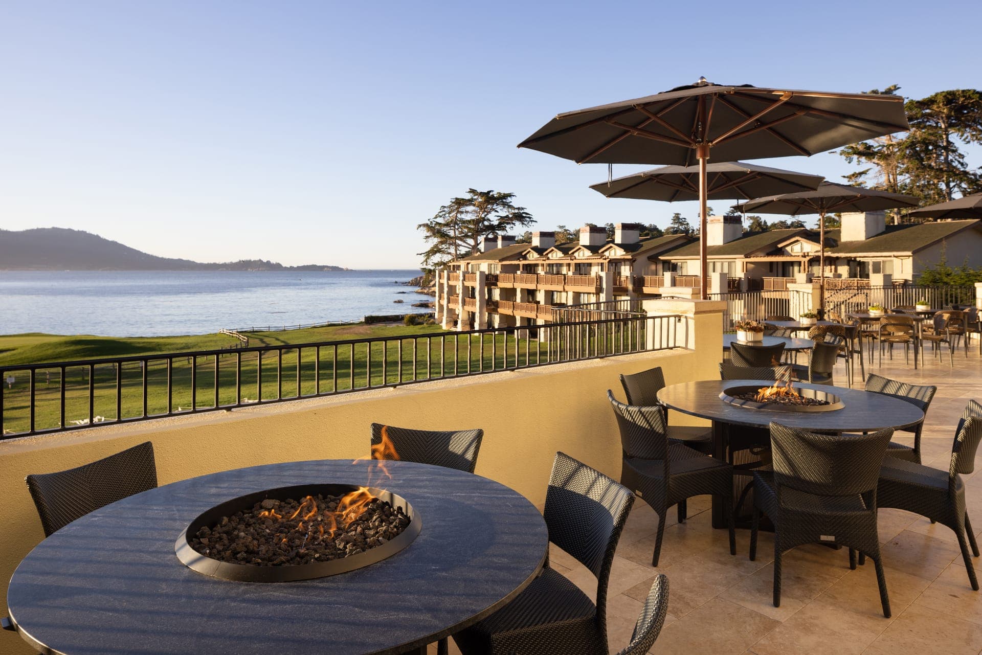 The Lodge at Pebble Beach balcony terrace at golden hour, firepit tables overlooking the 18th green and Carmel Bay