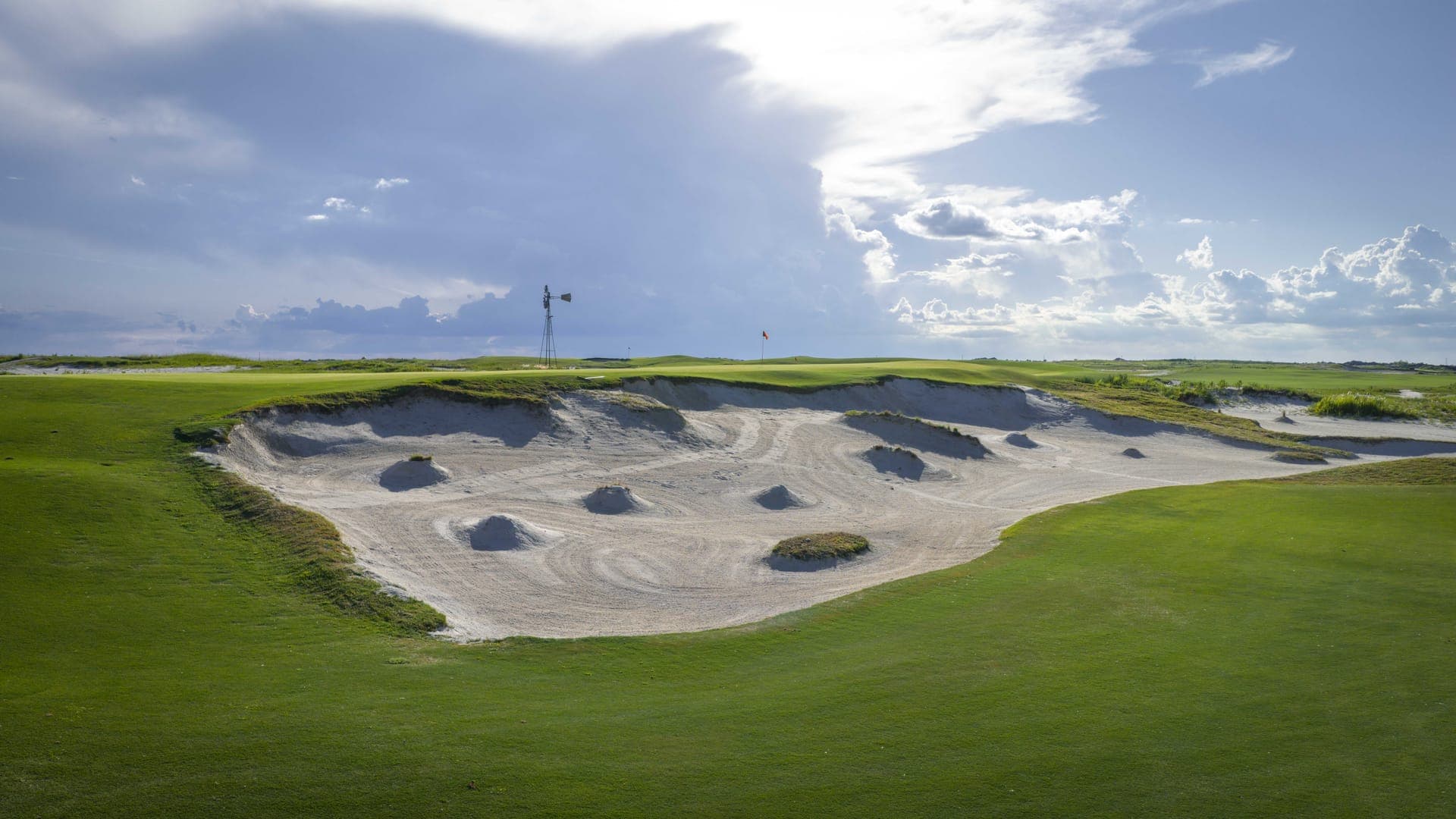 Massive bunker complex at Streamsong Black with native grass mounds inside the sand and a windmill on the horizon, designed by Gil Hanse
